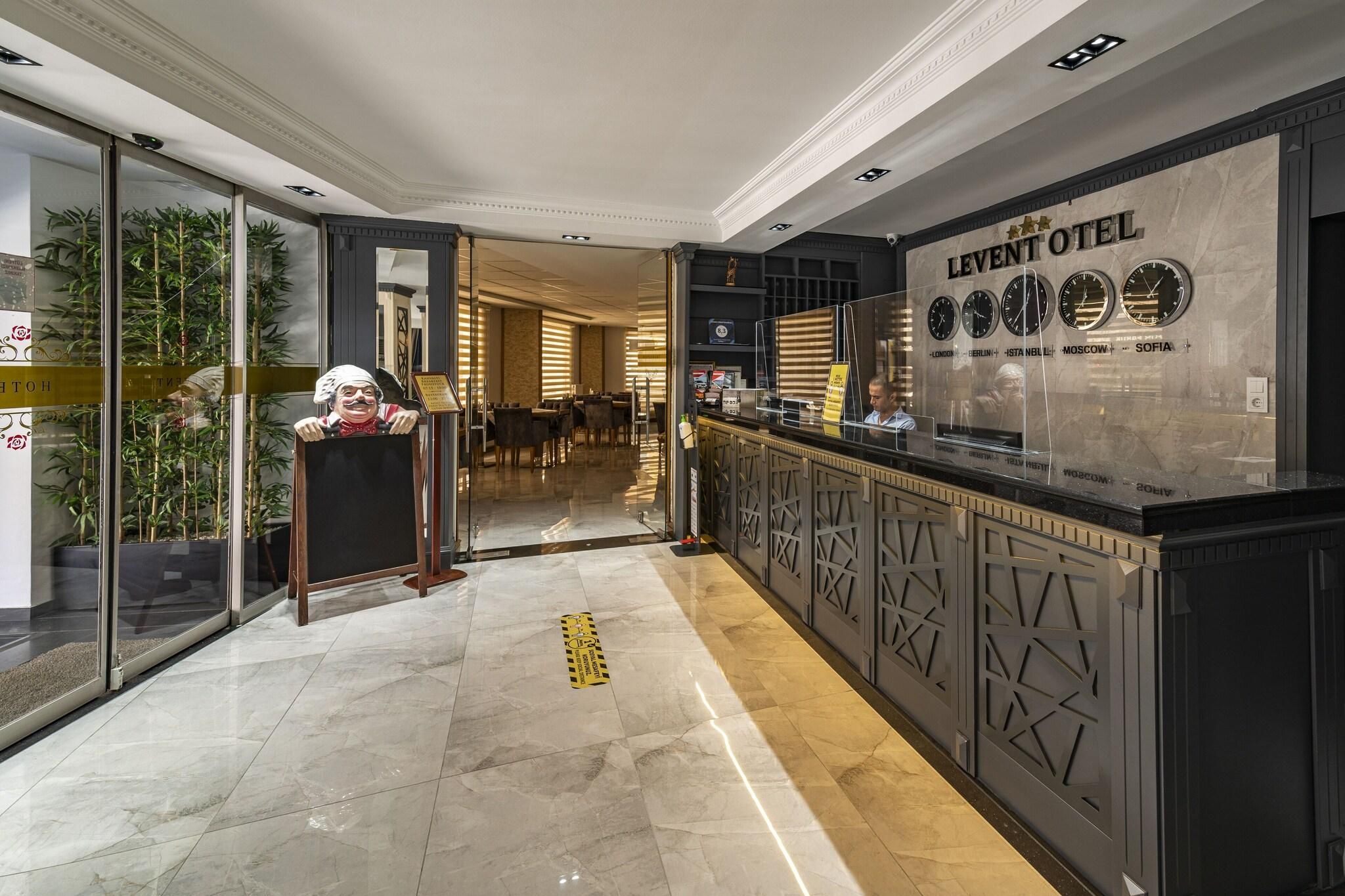 A hotel lobby with a reception desk, a glass partition, and a wall with clocks indicating different cities.