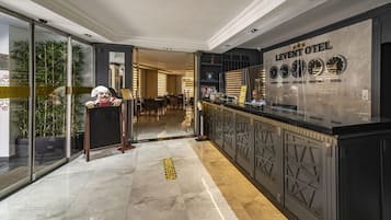 A hotel lobby with a reception desk, a glass partition, and a wall with clocks indicating different cities.