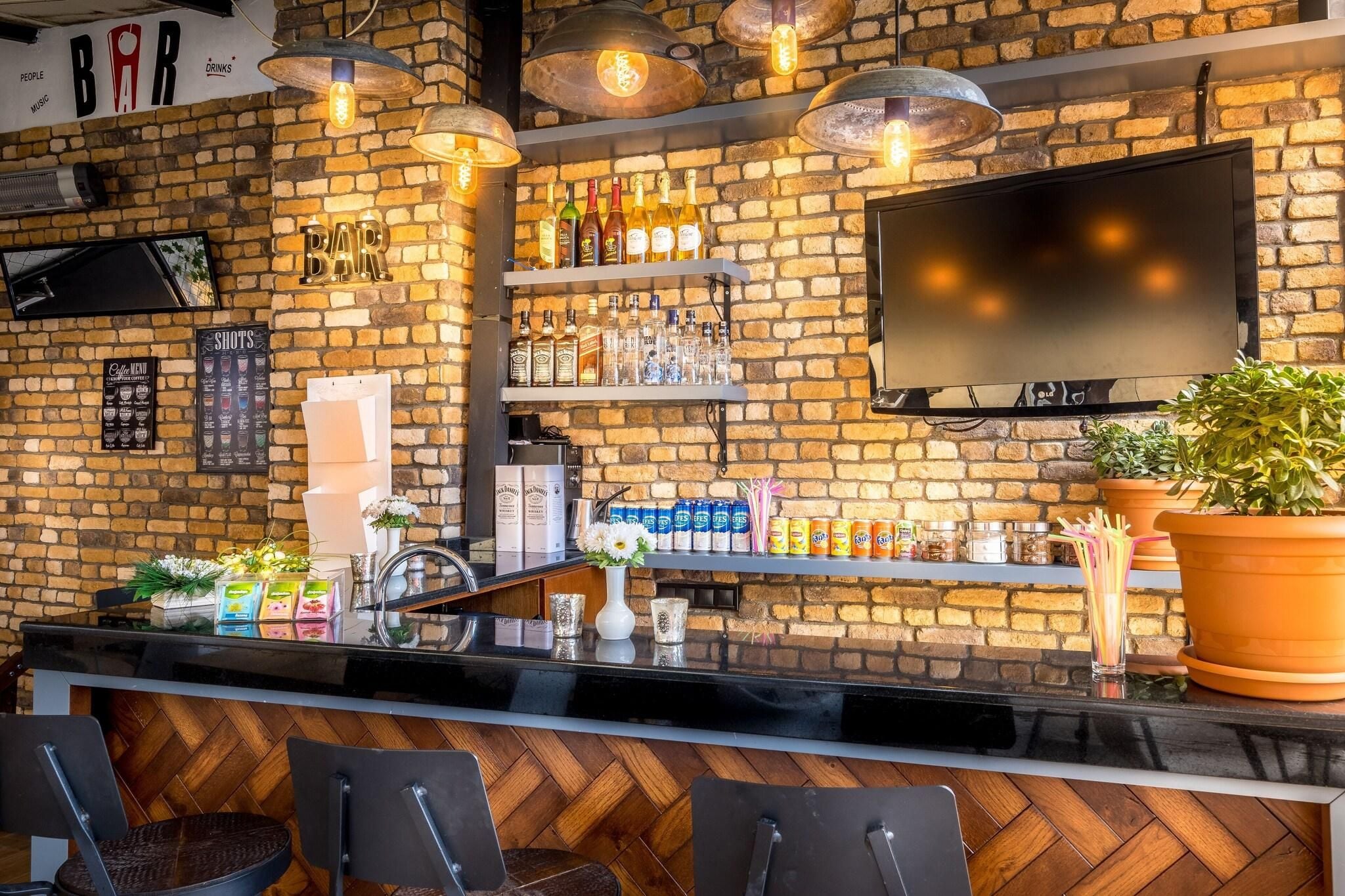 A bar with a brick wall, shelves of bottles, a TV, and a potted plant.