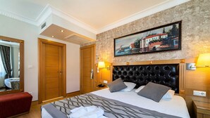 Quarto de hotel com uma cama grande, guarda-roupa de madeira, um quadro na parede e um banco vermelho.