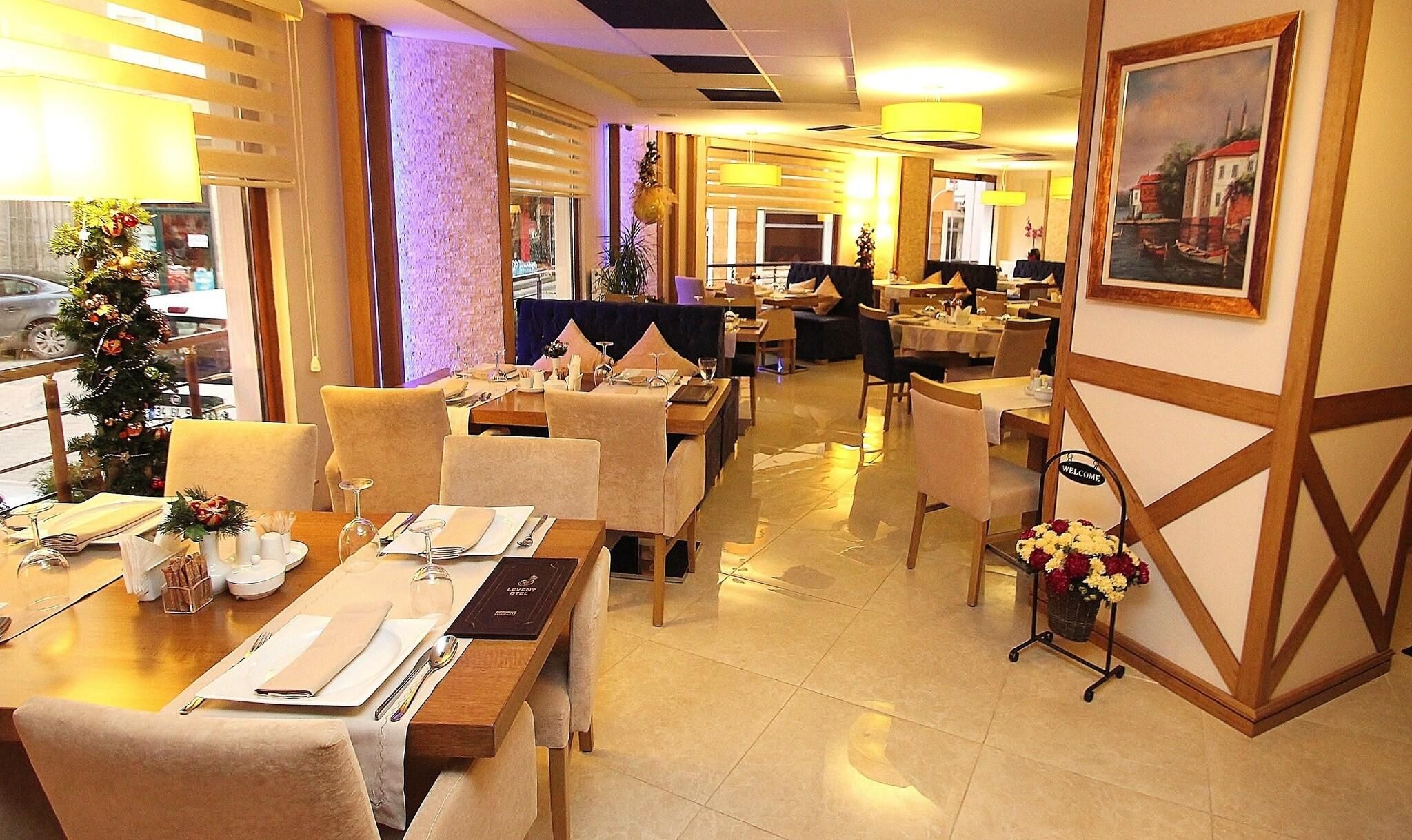 A hotel dining area with tables set for guests, a Christmas tree, and a painting on the wall.
