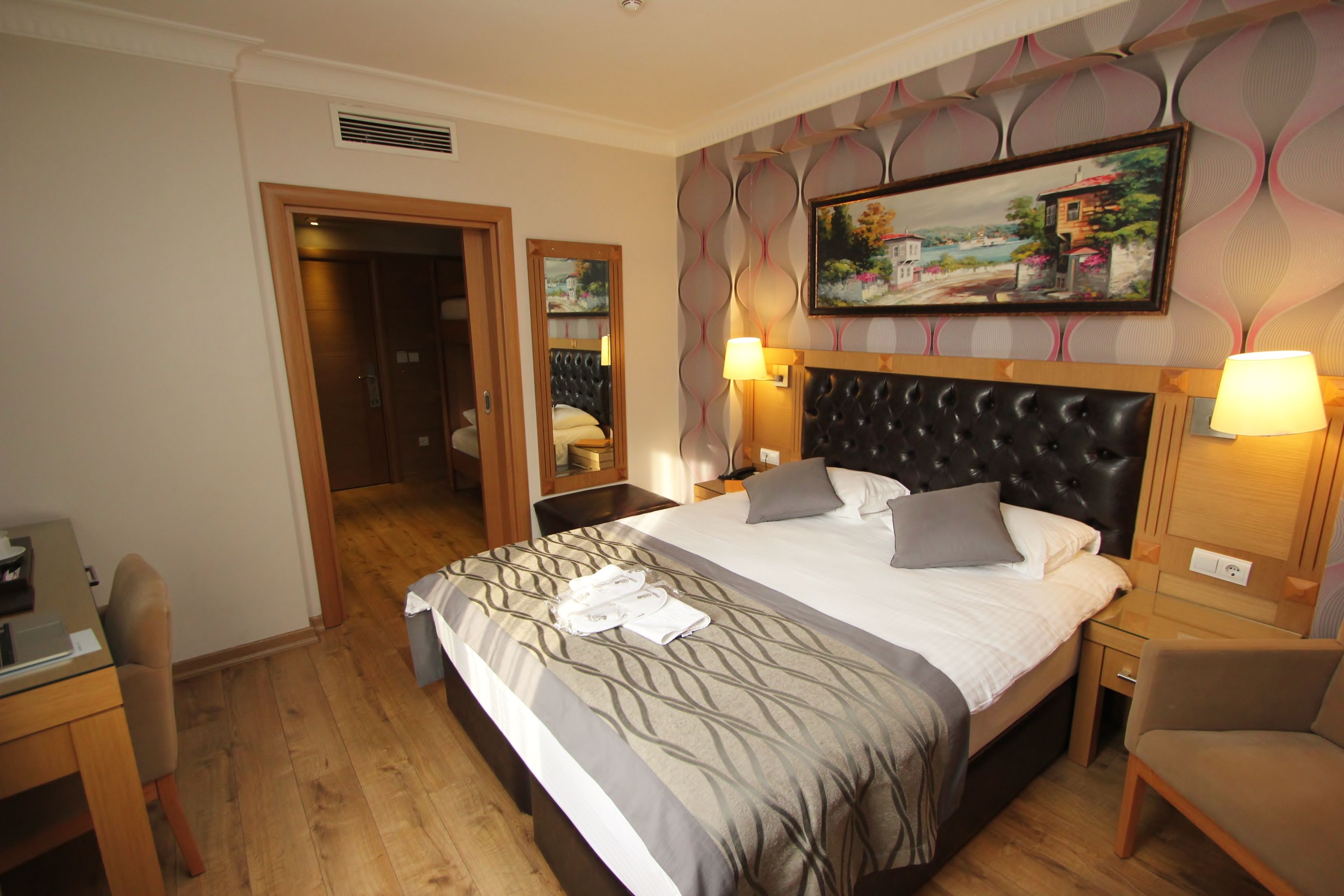 A hotel room with a large bed, two bedside tables, a desk, a chair, and a painting on the wall.