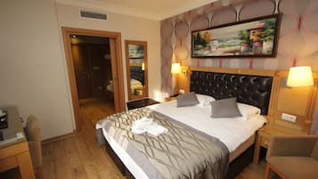 A hotel room with a large bed, two bedside tables, a desk, a chair, and a painting on the wall.