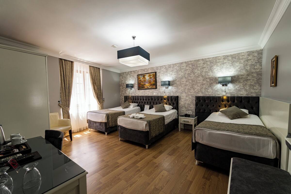 A hotel room with two beds, a desk, a chair, and a dining table.