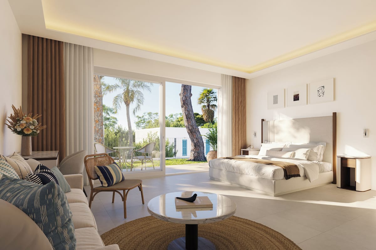 A modern hotel room with a large bed, a sofa, a dining table, and a view of palm trees and a building outside.