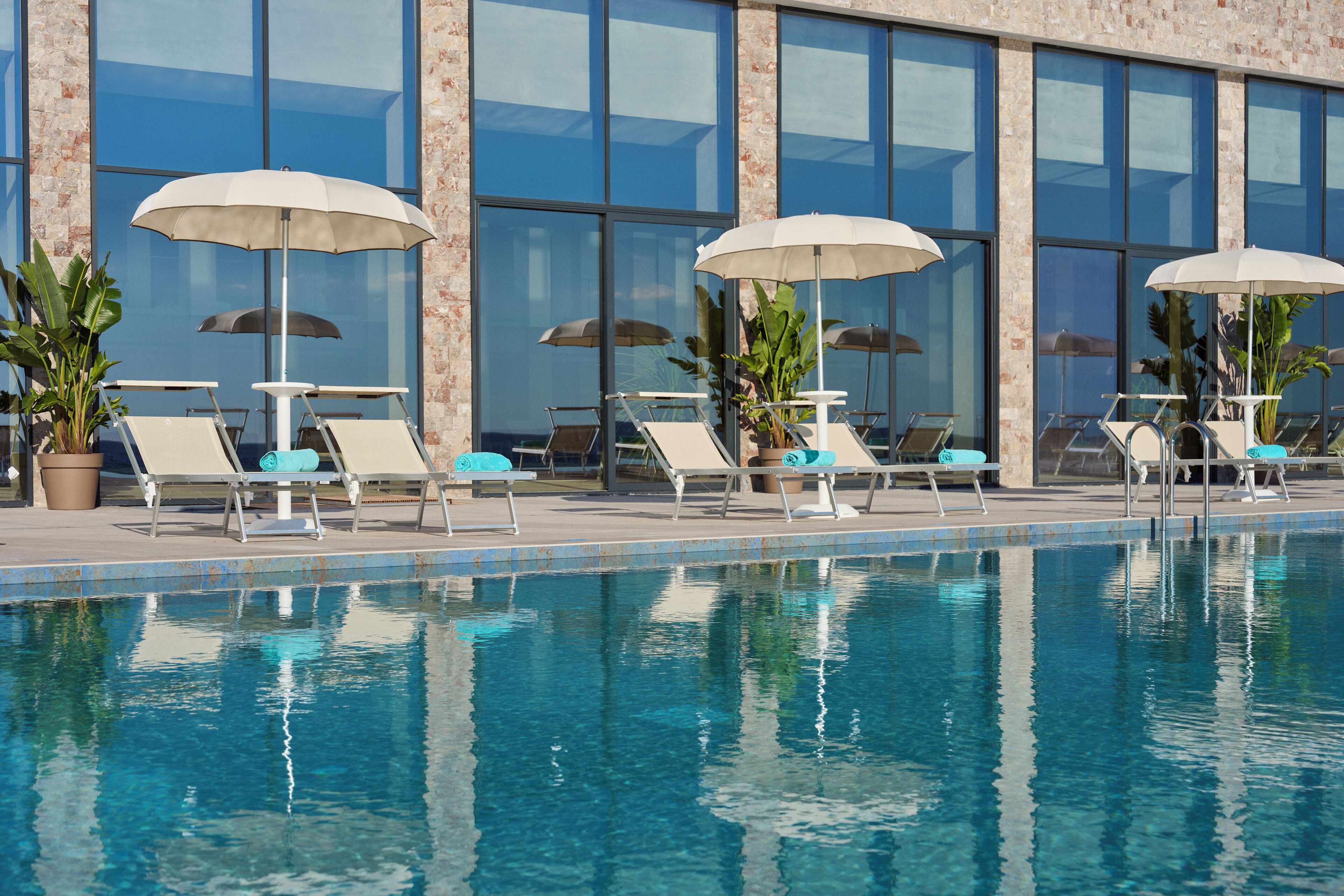 A swimming pool with lounge chairs and umbrellas, large windows, and a brick facade.