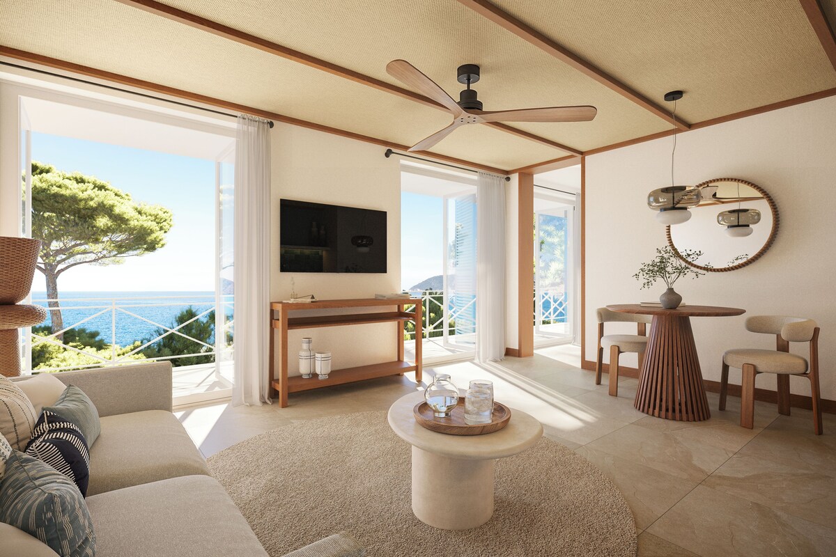 Ein geräumiges Wohnzimmer mit großem Fenster, Deckenventilator, rundem Couchtisch und Wand-Fernseher.