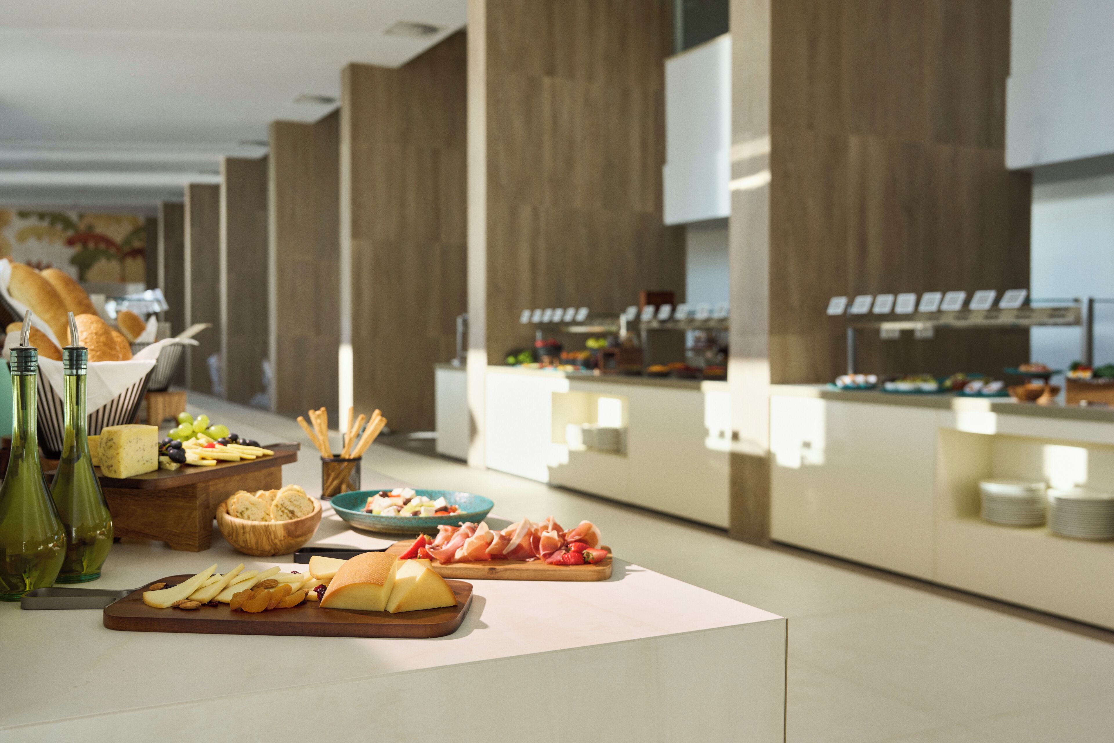 Montaje de bufé con diversos alimentos, como quesos, frutas y carnes, en una cocina moderna.