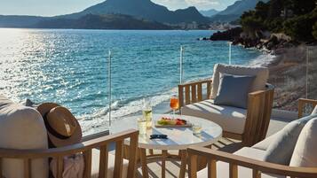 Una terraza frente al mar con una mesa redonda, dos sillas y vistas al mar y a las montañas.
