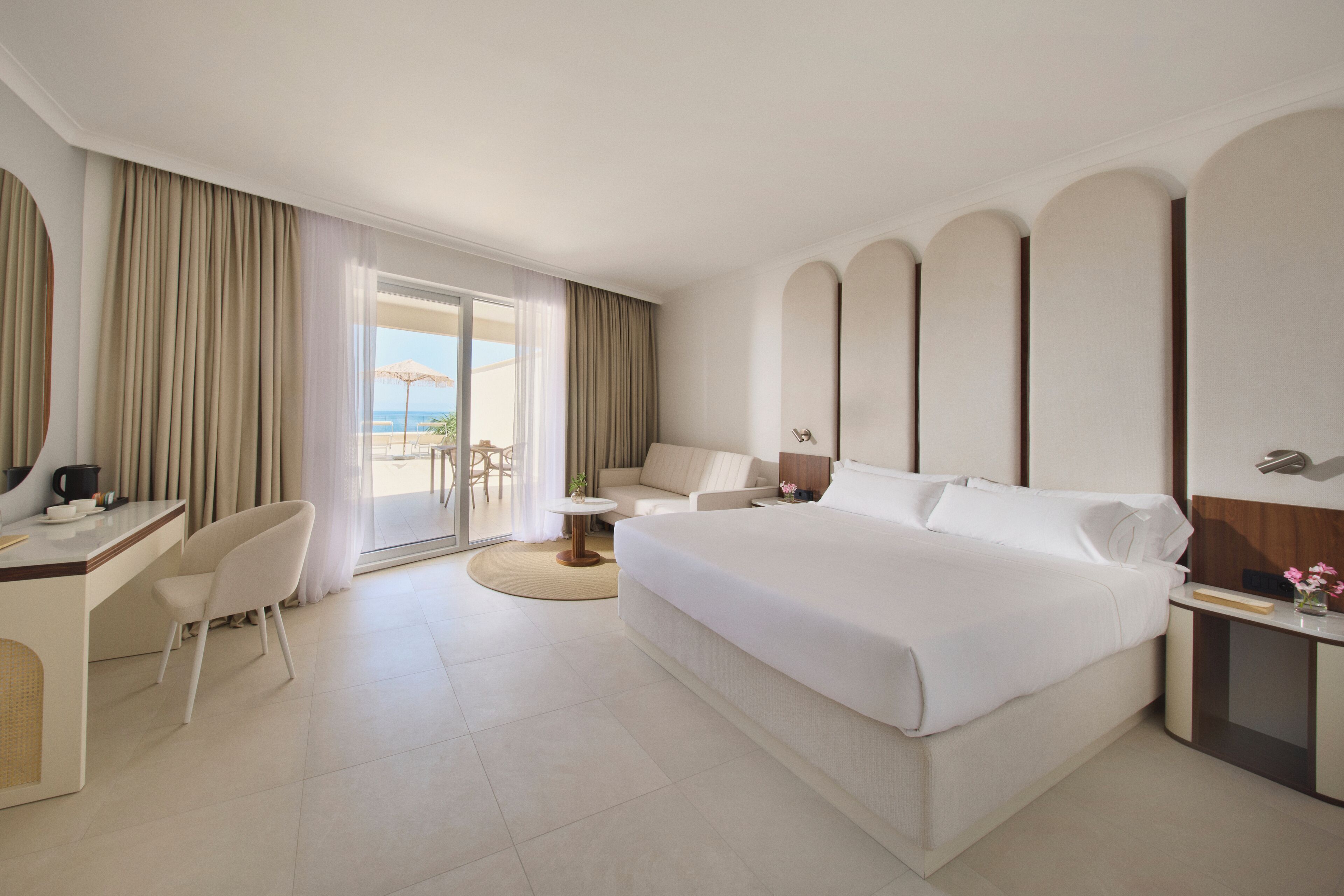 A hotel room with a bed, desk, chair, and a view of the beach.