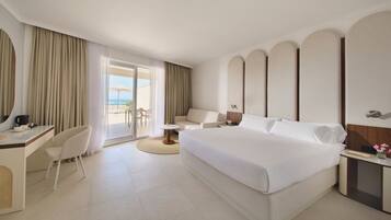 A hotel room with a bed, desk, chair, and a view of the beach.