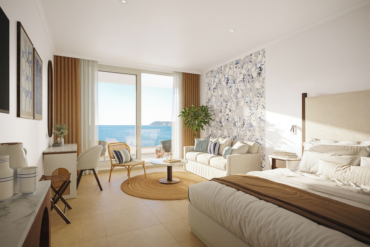 Una habitación de hotel moderna con una cama grande, un sofá, un escritorio y un balcón con vista al mar.