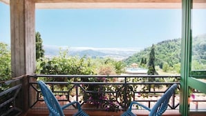 A wooden balcony with two blue chairs, a view of a lush valley, and a small pool with a gazebo.