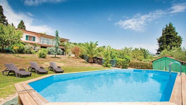 A rectangular swimming pool with a wooden deck edge, surrounded by a grassy area with three lounge chairs.