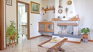 A living room with a fireplace, a dining table, and potted plants.