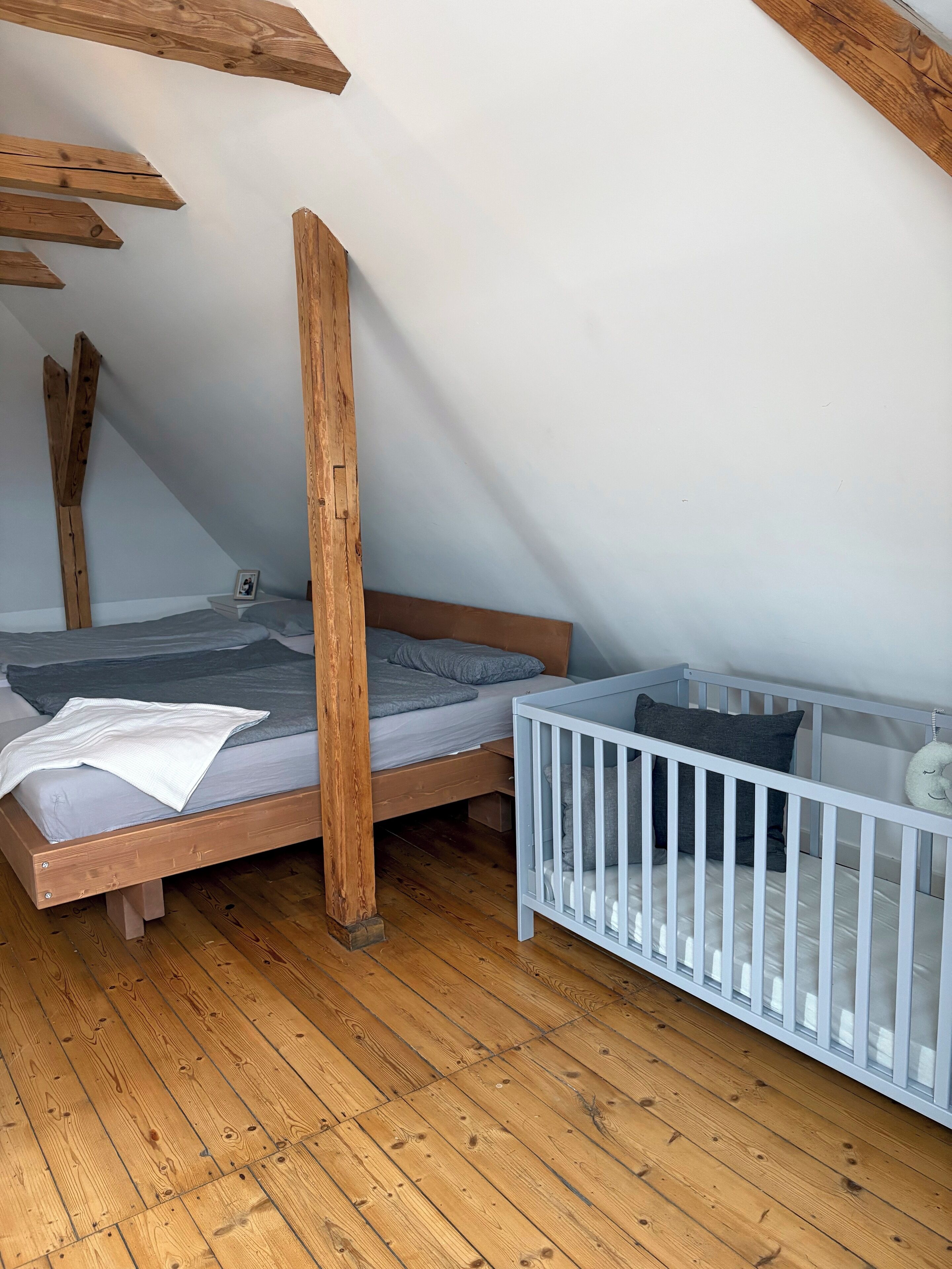 A bedroom with a wooden bed, a crib, and a sloped ceiling.