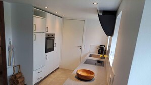 Una cocina compacta con muebles blancos, horno integrado, cafetera y un tazón de madera sobre la encimera.