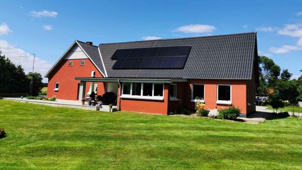 Una casa con fachada roja, techo negro y un panel solar en el techo.