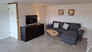Una sala moderna con televisor de pantalla plana, cómoda de madera oscura, sofá gris con cojines y dos cuadros enmarcados en la pared.