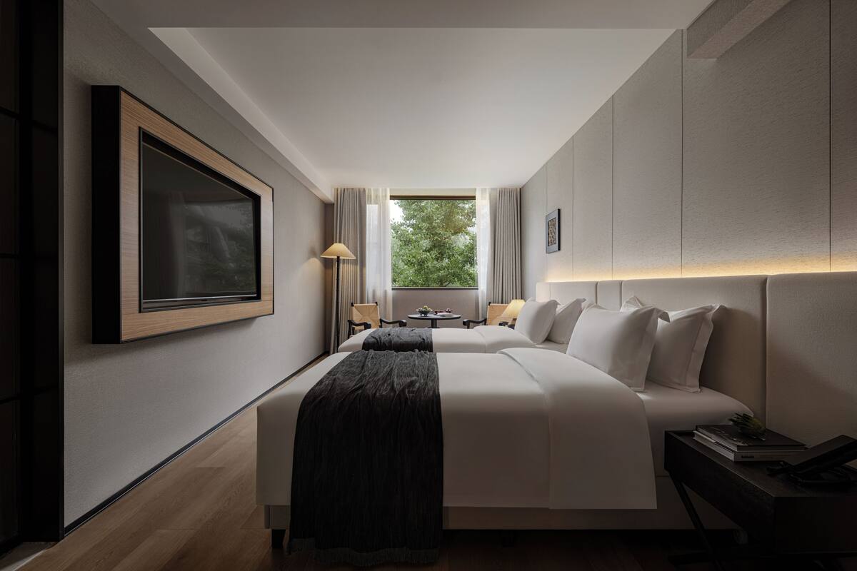 Et moderne hotelværelse med en stor seng, et skrivebord og udsigt til grøn vegetation gennem vinduet.