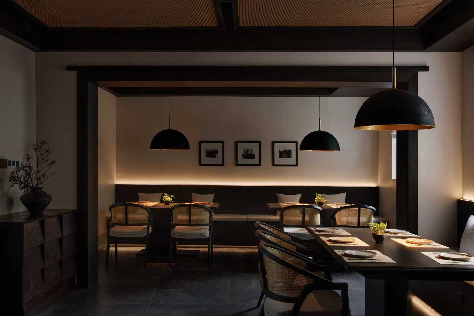 Een moderne eetruimte met een lange tafel, stoelen, hanglampen en ingekaderde foto's aan de muur.
