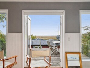 Eine geöffnete Tür führt zu einer Terrasse mit Tisch und Stühlen, mit Blick auf eine Landschaft, in der sich ein Gebäude in der Ferne befindet.