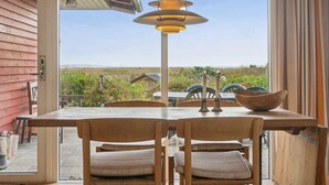 Un espace repas comprenant une table et des chaises, un luminaire suspendu et une vue sur l’extérieur.