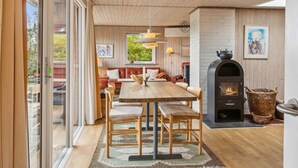 Une cuisine moderne dotée d’un poêle à bois, un coin repas avec une table et des chaises en bois, et un espace salon confortable avec un canapé et des coussins.