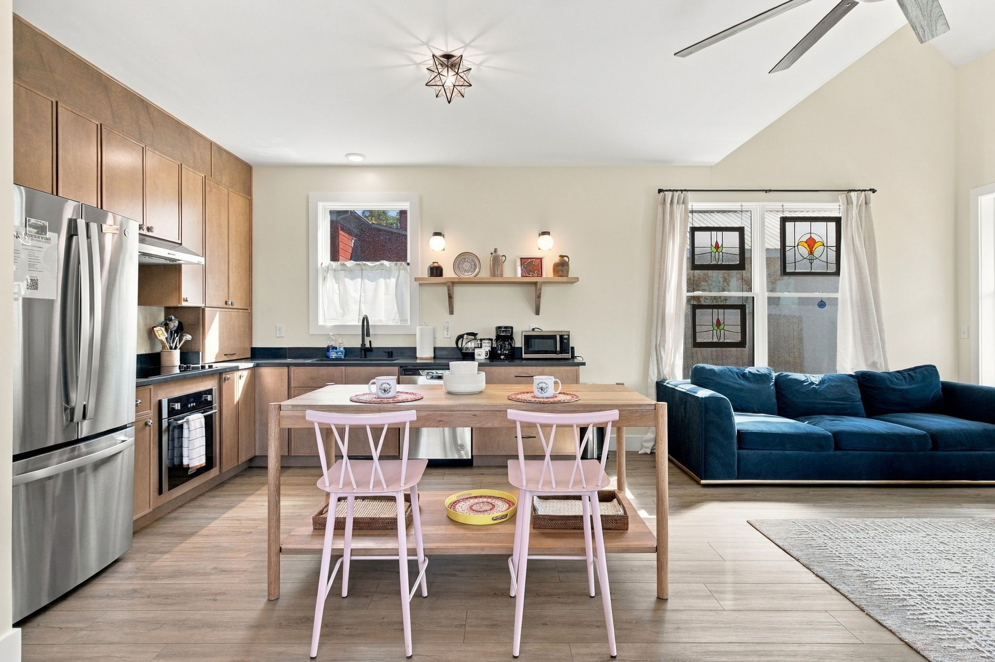 A modern kitchen with a dining area, a blue sofa, and a large window with curtains.