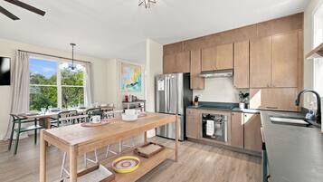 A modern kitchen with wooden cabinets, a stainless steel refrigerator, and a dining area with a wooden table and chairs.