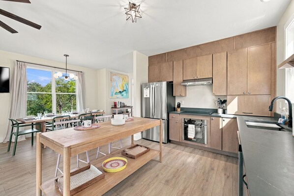 Una cocina moderna con armarios de madera, un refrigerador de acero inoxidable y una zona de comedor con mesa y sillas de madera.