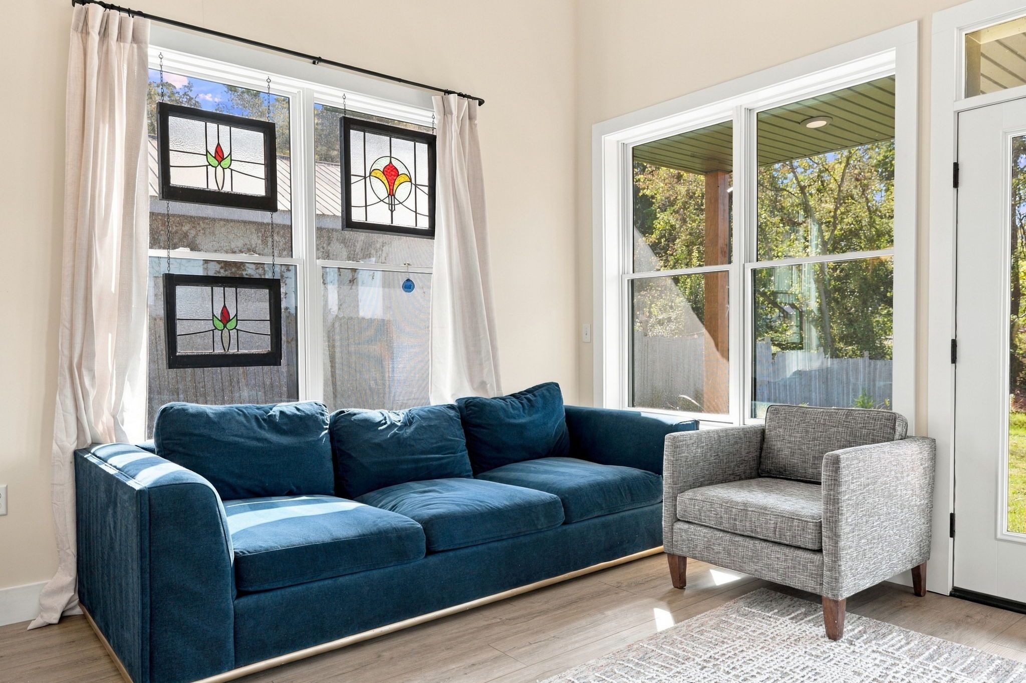 A living room with a blue sofa, a grey armchair, and a large window with curtains.