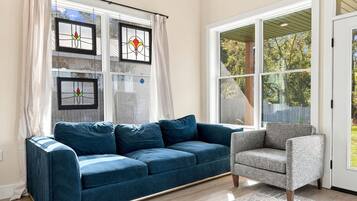 A living room with a blue sofa, a grey armchair, and a large window with curtains.