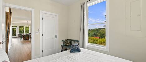 Un dormitorio con una cama grande, una ventana con vistas a la vegetación y una puerta que conduce a un comedor.