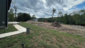 Un chantier de construction avec une dalle de béton, une pile de bois et une remorque rouge en arrière-plan.