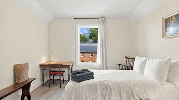 A bedroom with a bed, a desk, a chair, a window, and a painting on the wall.