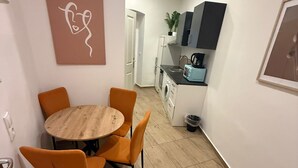 A compact living space with a dining area featuring a round wooden table and orange chairs, a kitchenette with modern appliances, and a minimalist decor. - Bright 1BR Apt Near Top Vienna Sights (Vienna)