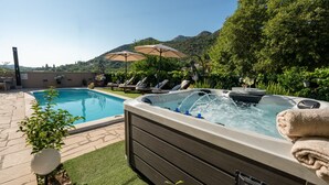 Un jardin avec une piscine, un jacuzzi, des chaises longues et une vue imprenable sur les montagnes.