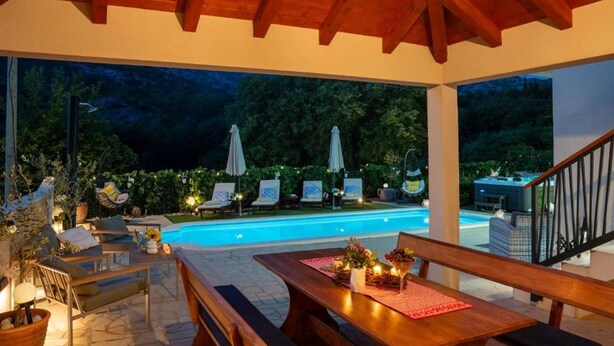 Un espace extérieur avec une piscine, des chaises longues et des parasols, une table en bois avec un set de table rouge, et un escalier menant à un niveau supérieur.