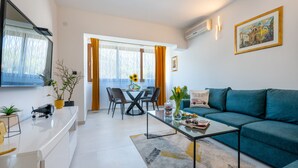 Un salon moderne comprenant un canapé, une table basse, un coin repas avec des chaises et un téléviseur fixé au mur.