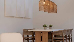 Un espace repas moderne avec une table en bois, des chaises en osier et un luminaire suspendu.