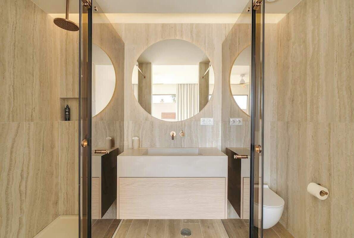 A modern bathroom with a glass-enclosed shower, a central sink, and two mirrors.