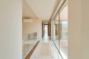 A modern hotel hallway with a glass door leading to a balcony, a wooden floor, and a light-colored rug. - 4BR Villa w/ Private Pool | Salgados | DA’Home (Albufeira)