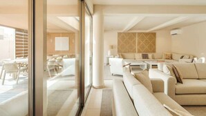 A modern hotel room with a large glass door leading to a balcony, a seating area with sofas and a coffee table, and a large woven wall decoration. - 4BR Villa w/ Private Pool | Salgados | DA’Home (Albufeira)