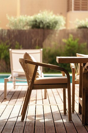 A wooden deck with a wicker chair and a table, overlooking a swimming pool. - 4BR Villa w/ Private Pool | Salgados | DA’Home (Albufeira)