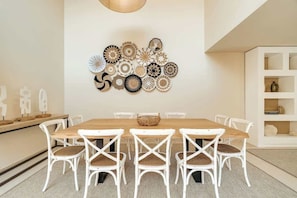 A dining area with a wooden table and white chairs, a wall decorated with circular patterns, and a white shelving unit with decorative items.