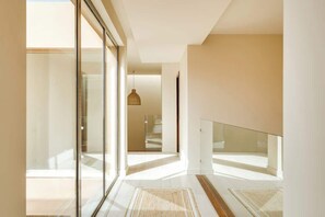 A modern interior with a glass door leading to a balcony, a hanging light fixture, and a staircase.