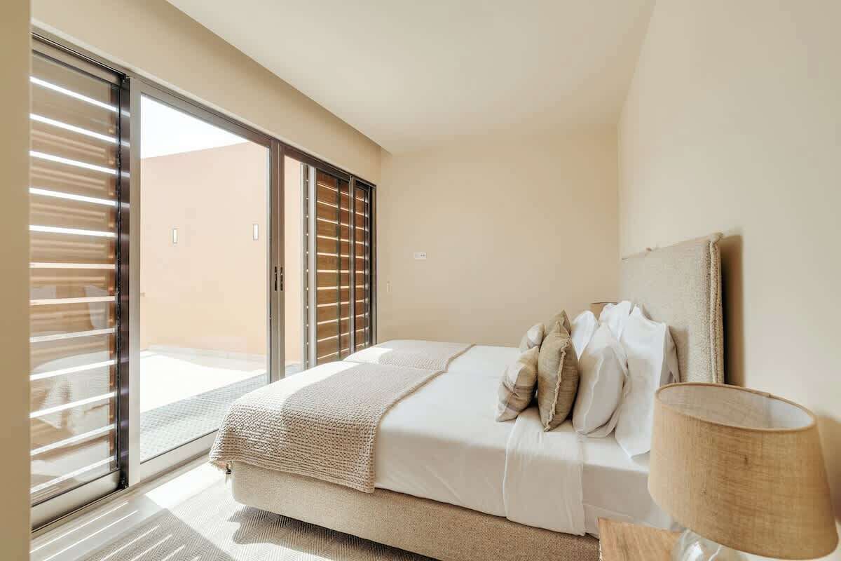 A bedroom with a bed, a nightstand, a lamp, and a sliding glass door leading to a balcony.
