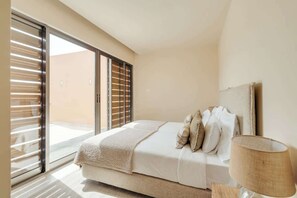 A bedroom with a bed, a nightstand, a lamp, and a sliding glass door leading to a balcony.