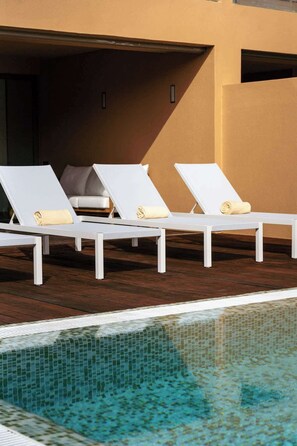 Un espace aménagé au bord de la piscine, avec trois chaises longues blanches, chacune agrémentée d’une serviette.